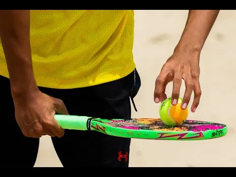 Jogador segurando raquete de beach tennis com bola apoiada, demonstrando controle e preparação para saque