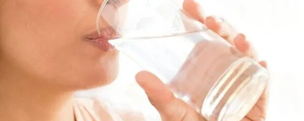 Pessoa bebendo água em copo transparente, destacando o ato de hidratação saudável.