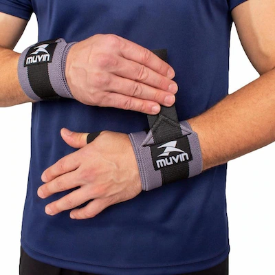 Pessoa ajustando munhequeira esportiva cinza com alça preta e suporte para polegar, vestindo camiseta azul, em ambiente de treino.