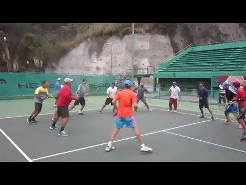 Grupo de jogadores em quadra de tênis realizando treino coletivo, com raquetes em mãos e ambiente esportivo ao ar livre.