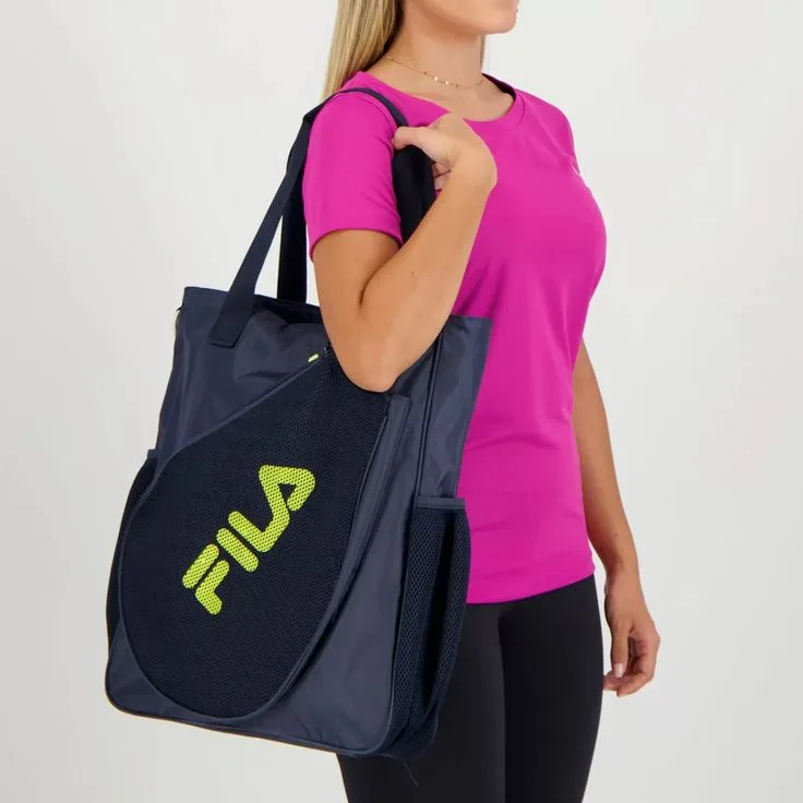 Pessoa usando camiseta rosa e segurando bolsa esportiva azul marinho da marca FILA com logo em destaque.