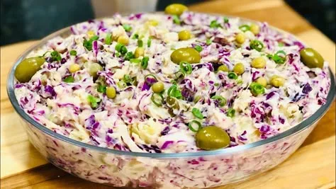 Salada cremosa em tigela de vidro com repolho roxo e branco, ervilhas, cebolinha picada e azeitonas verdes.