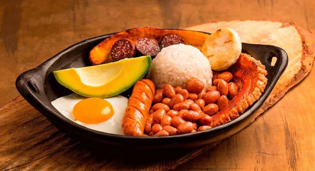 Prato típico colombiano Bandeja Paisa servido em cerâmica preta com arroz, feijão, ovo frito, abacate, linguiça, torresmo, banana frita, morcilla e arepa.