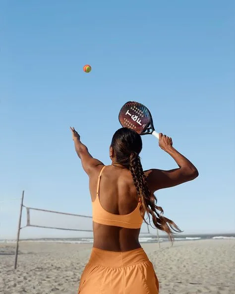 Jogador de beach tennis em quadra de areia, vestindo roupa esportiva laranja e golpeando bola com raquete KOW.