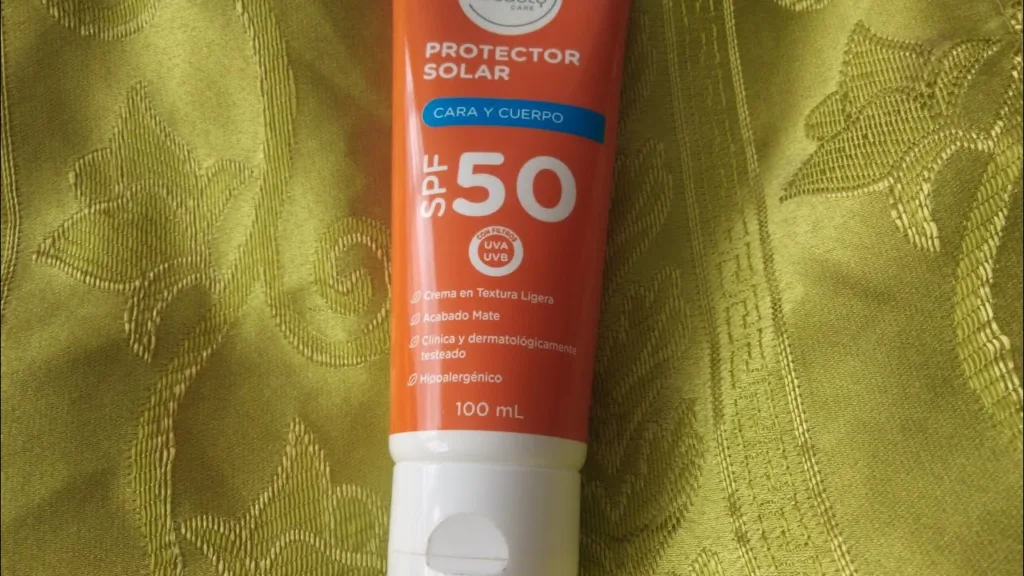 Protetor solar FPS 50 em tubo laranja e branco sobre tecido verde estampado, indicado para rosto e corpo com proteção UVA e UVB.