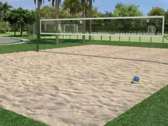 Quadra de vôlei de areia em parque ao ar livre, com bola sobre a areia e árvores ao fundo.