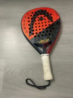 Raquete de padel Head Delta com design em vermelho e preto, formato de lágrima e furos simétricos na face. O logotipo da Head aparece em destaque na parte superior, e o nome “Delta” está impresso em amarelo próximo à base. O cabo é branco com alça preta.