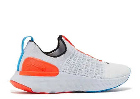 Tênis de corrida Nike React Phantom Run Flyknit slip-on em branco e cinza claro, com detalhes laranja brilhante no calcanhar, calça azul-céu e sola de espuma React branca sobre fundo neutro.