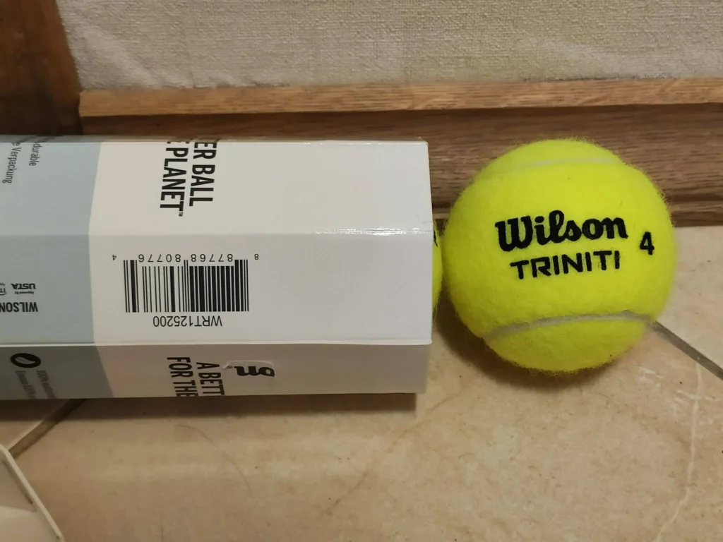 Bola de tênis Wilson Triniti número 4 ao lado da embalagem sustentável com o texto “A Better Ball for the Planet”.