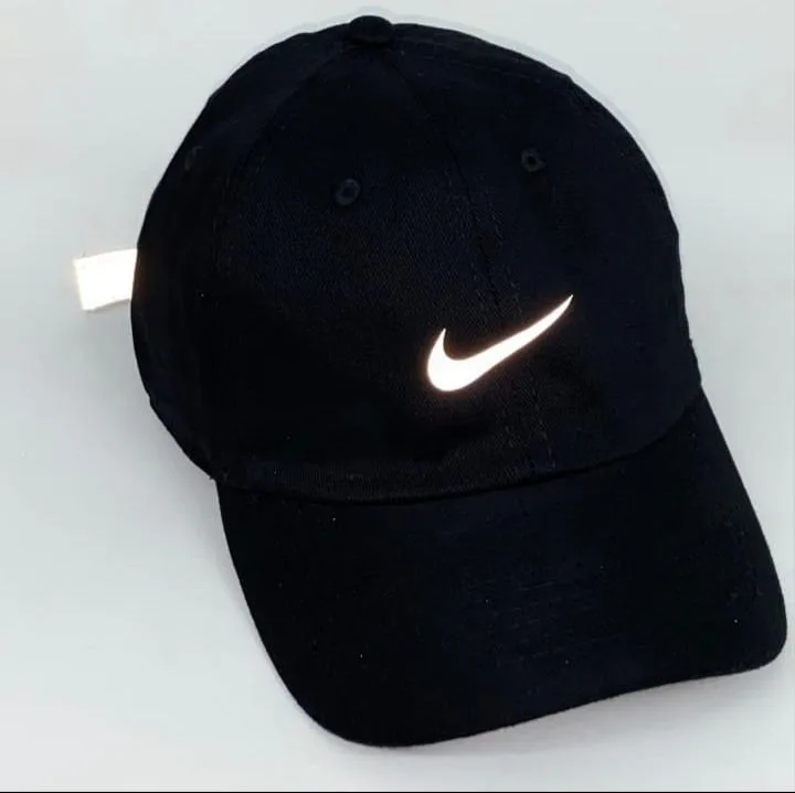 Boné preto da Nike com o icônico logotipo “Swoosh” branco refletivo na parte frontal, exibido sobre fundo claro.