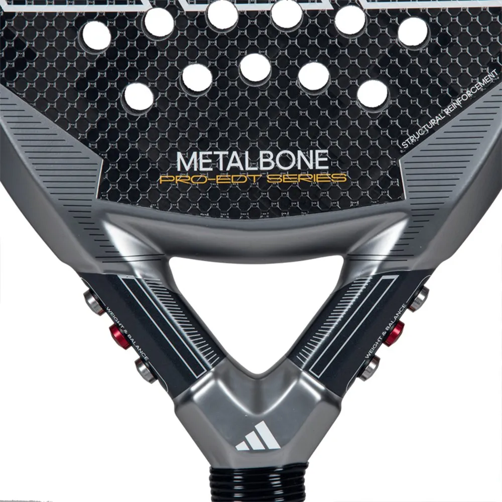 Close-up da raquete de padel Adidas Metalbone Pro EDT Series, mostrando detalhes técnicos da estrutura em preto e cinza com padrão hexagonal e furos circulares. O nome “METALBONE” aparece em branco e “PRO EDT SERIES” em dourado, com o logotipo Adidas na base.