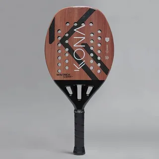 Raquete de beach tennis Kona Maverick Wood com acabamento em tom amadeirado, detalhes em preto e furos simétricos na face, exibindo o nome “KONA” em letras brancas verticais e cabo preto com grip texturizado.