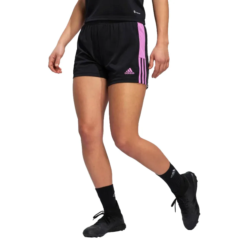Mulher vestindo shorts esportivo Adidas preto com detalhes em rosa nas laterais e três listras características da marca, combinando com meias e tênis pretos, ideal para treinos e esportes de areia.