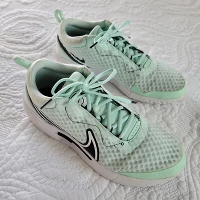 Par de tênis esportivos Nike em tom verde menta sobre uma colcha branca, destacando o design moderno e o tecido respirável.