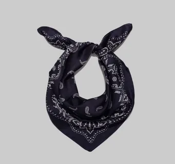 Bandana preta com estampa clássica paisley em branco, amarrada em formato triangular com nó na parte superior, sobre fundo cinza neutro.